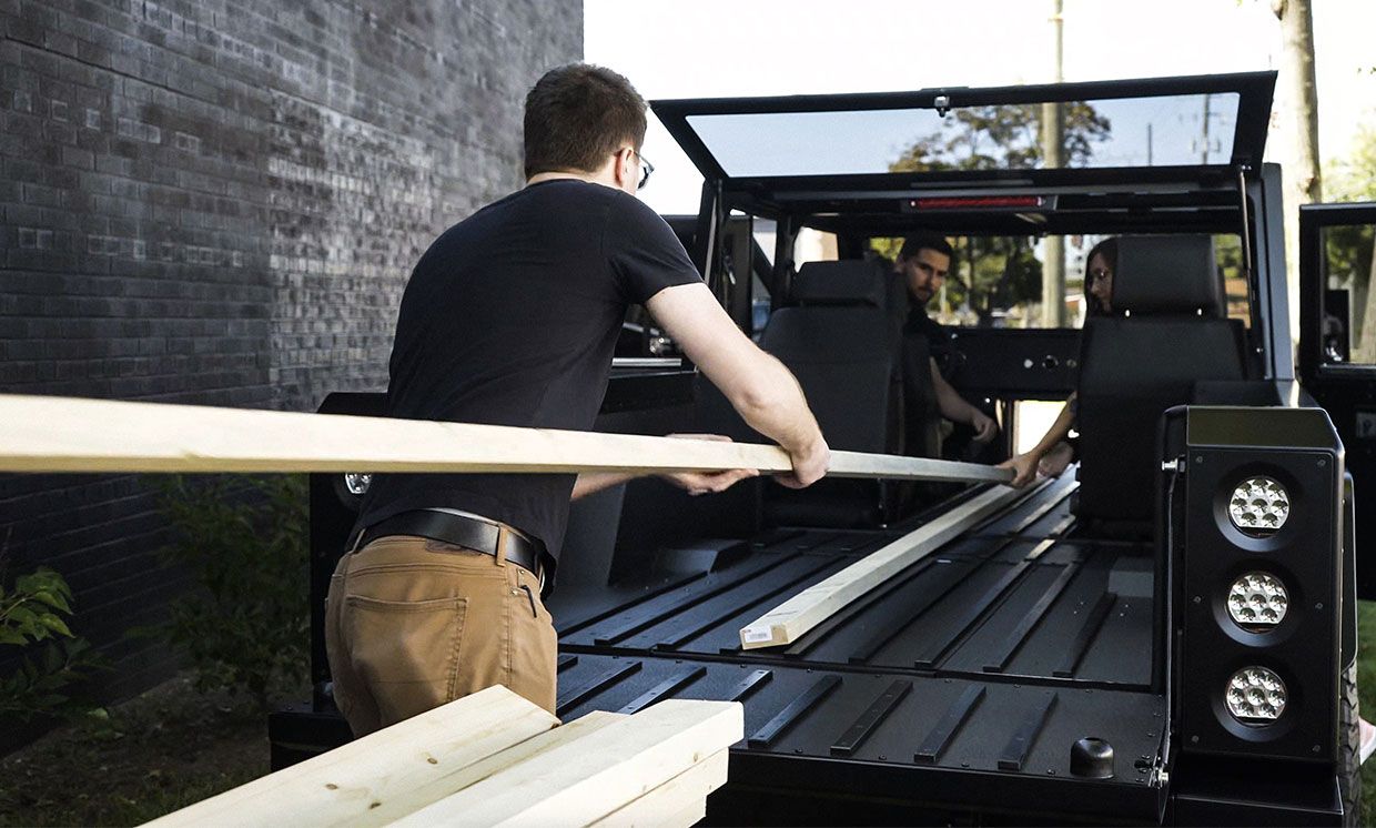 People load long pieces of lumber into the Bollinger Motors' B2 truck.