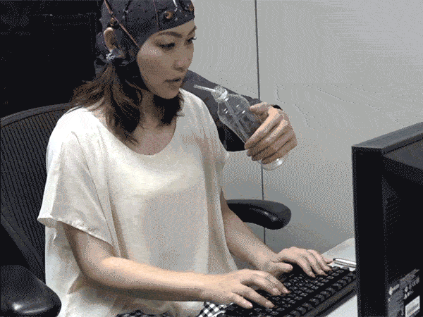 Gif showing a woman wearing the BMI electrode cap while typing with two hands and controlling the robotic "third" arm to give her water.
