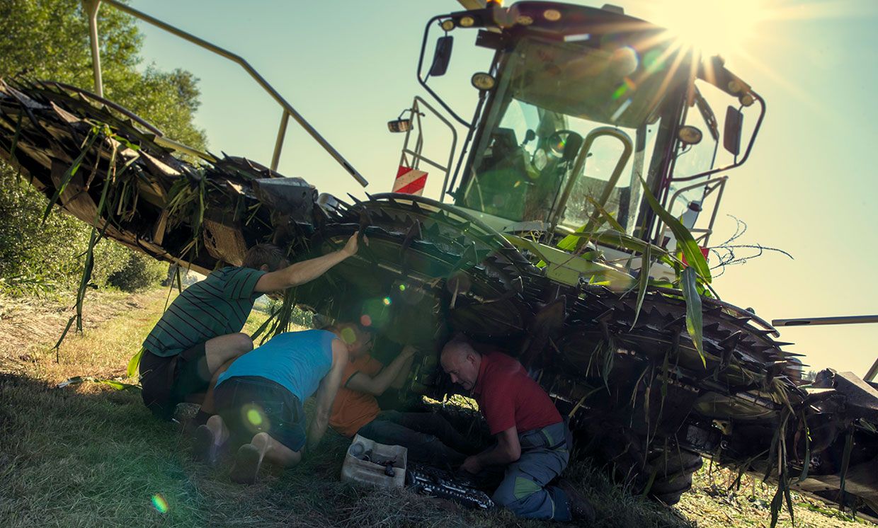 Four people working on a repair under a combine harvester.