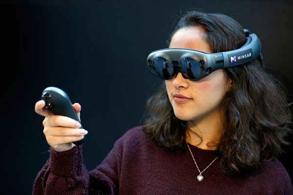 Photo of a woman wearing goggles and holding a controller. 