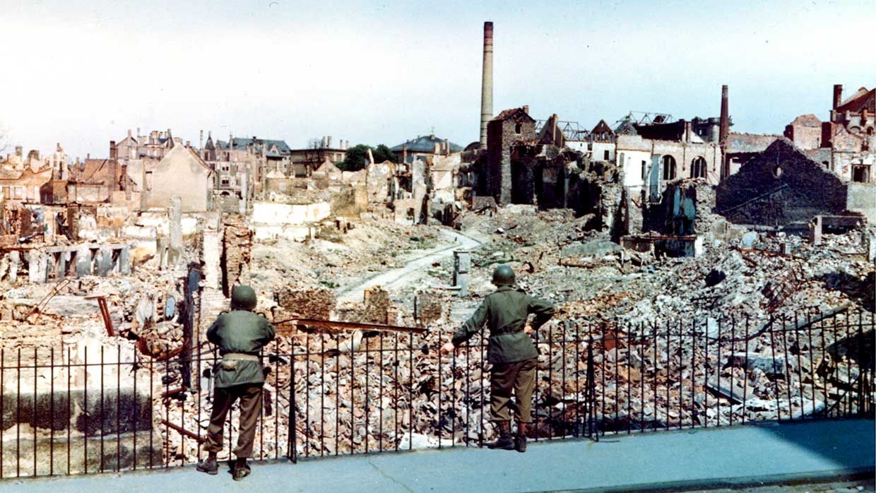 Two American soldiers stand behind a fence and survey the damage sustained during a saturation bombing raid on the city of Darmstadt, Germany, 1945. The raid, conducted on September 11 & 12, 1944 by British Royal Air Force Bomber Command, resulted in thousands of deaths, and rendered more than half the city's inhabitants homeless.