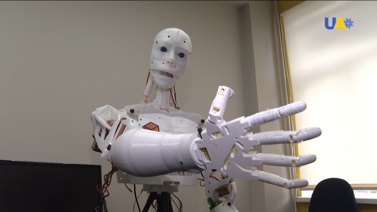 A 3D-printed humanoid robot looks toward the camera with an outstretched arm and hand
