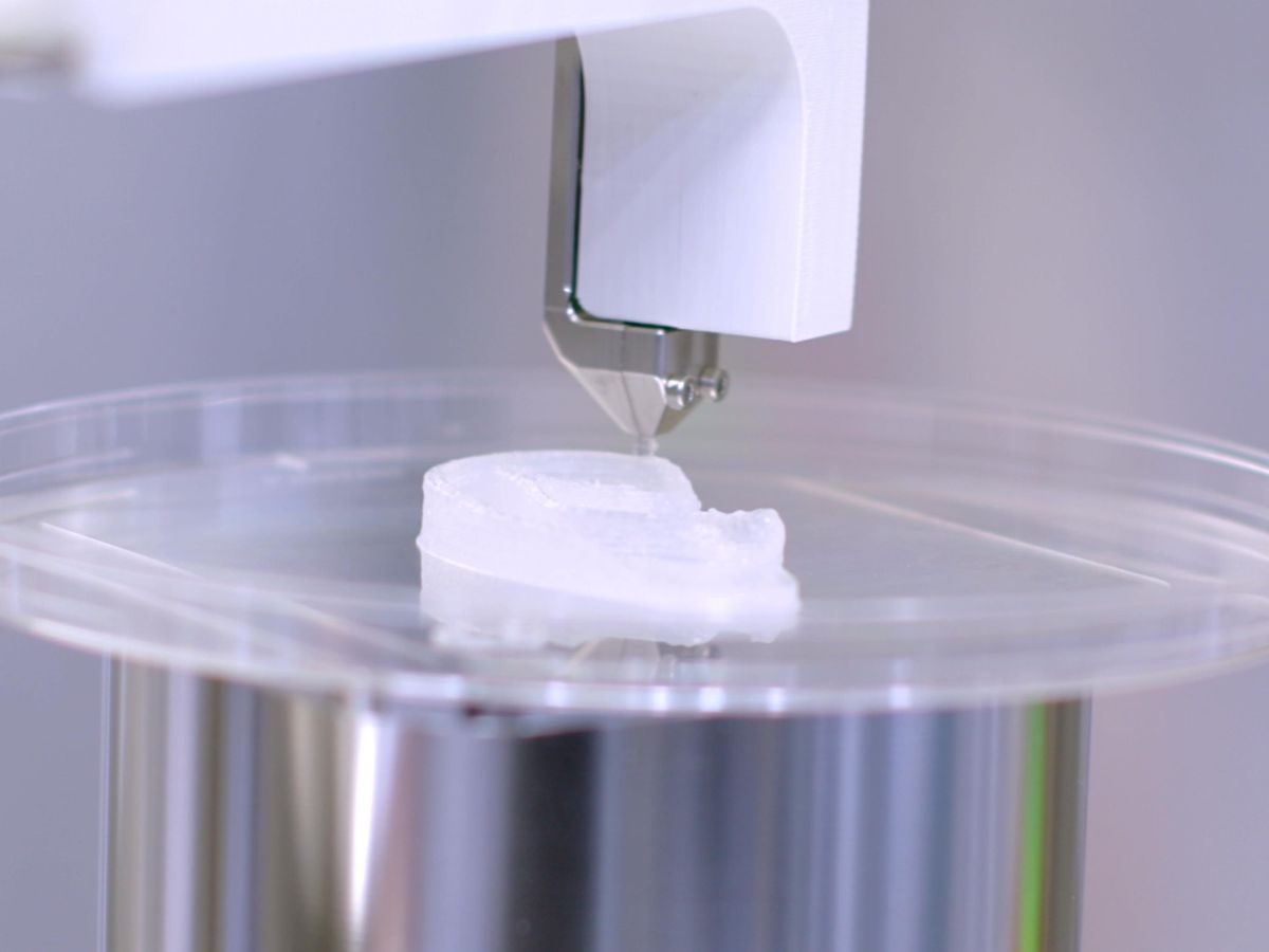 A 3D printer head is shown performing additive manufacturing of an outer ear in a petri dish. 