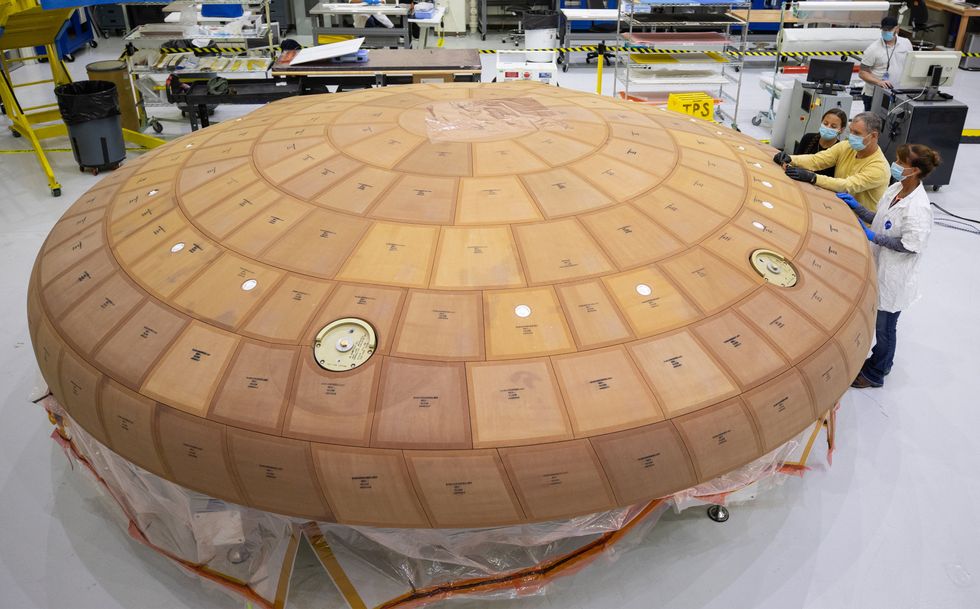 A big orange disc, curved downwards at the edge and tiled with rectangular or trapezoidal figures, is shown with three workers alongside, giving a sense of scale.