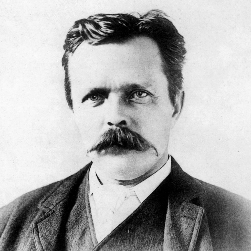 A black and white headshot of a man with a large mustache.