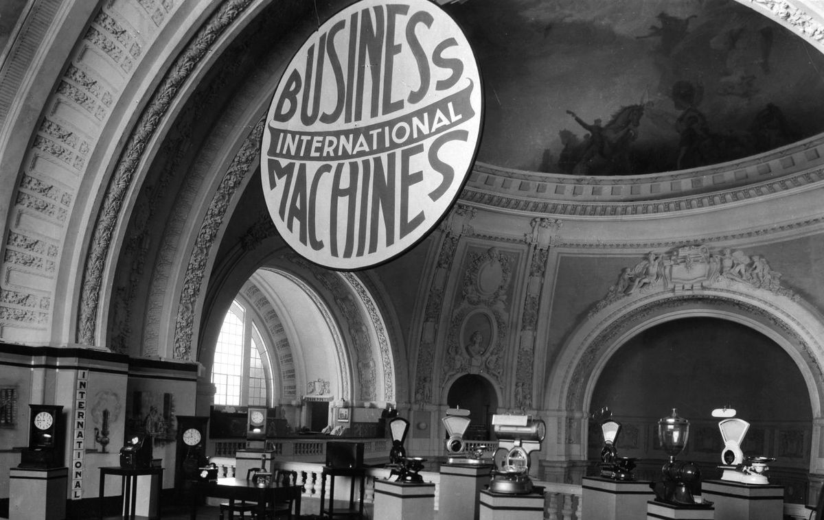 A black and white photo of a domed gallery with vintage machines displayed and a round sign that says International Business Machines.