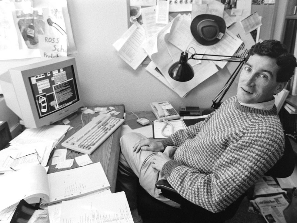 A black and white photo of a man in a checkered sweater sitting in front of an old computer.