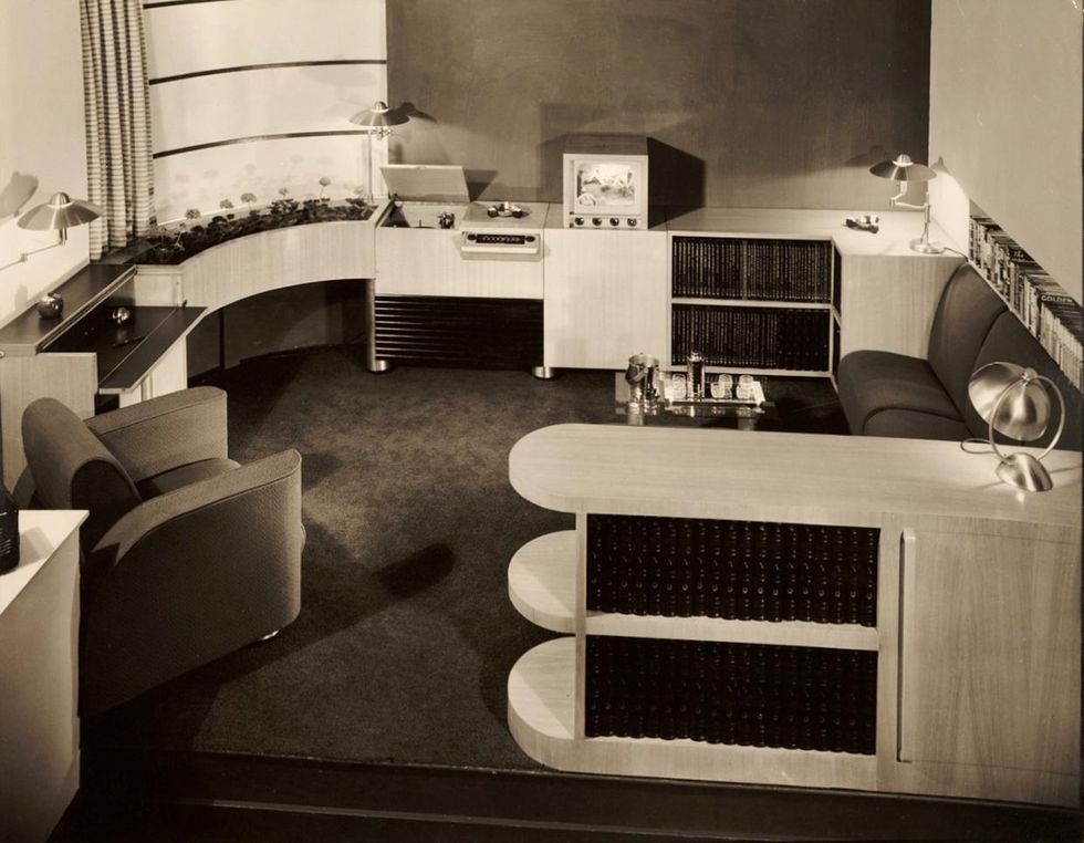 A black and white photo of a stylish art deco living room with a phonograph and television set. 