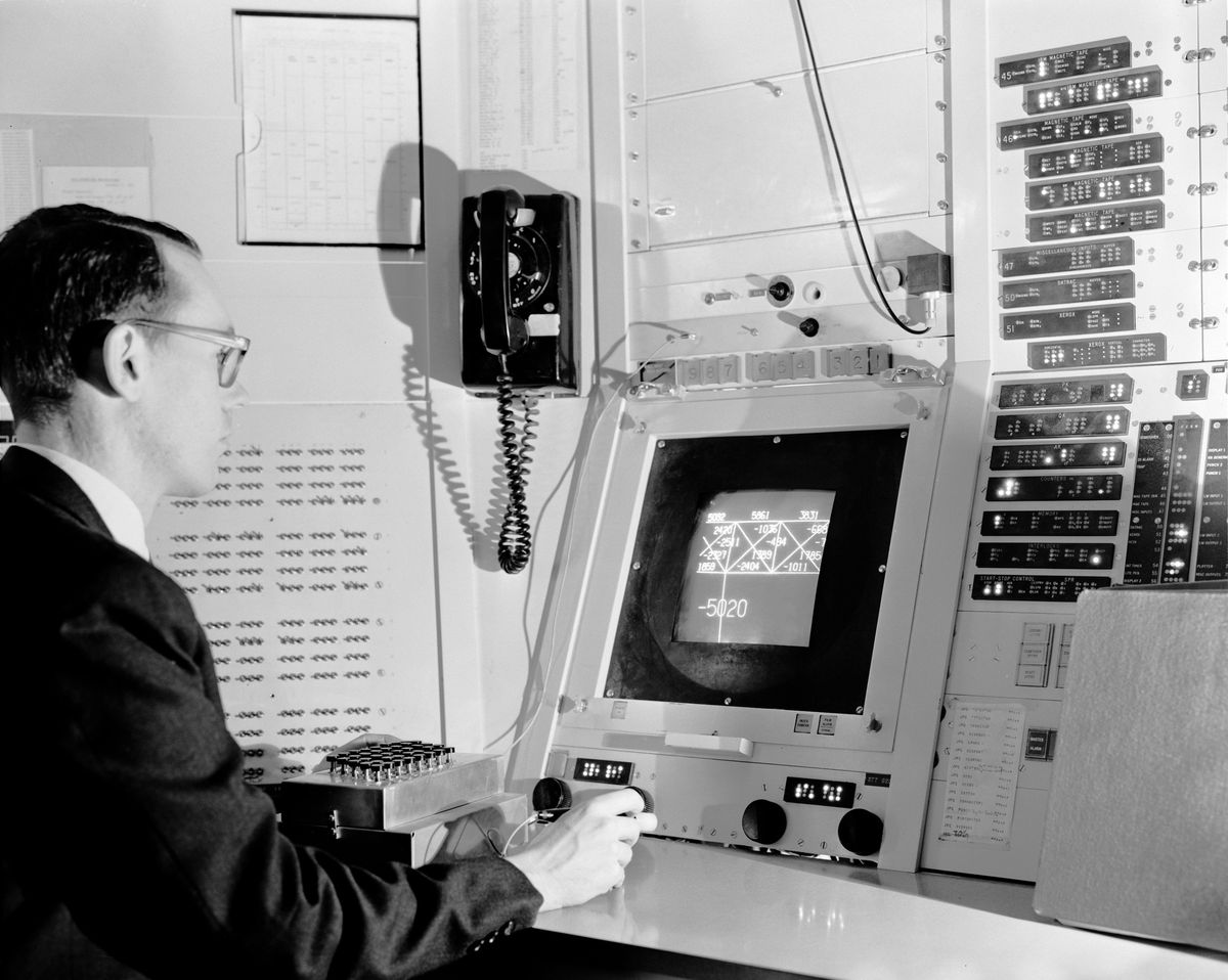 A black and white photo of a young man sitting in front of a CRT screen that has lines and numbers on it.
