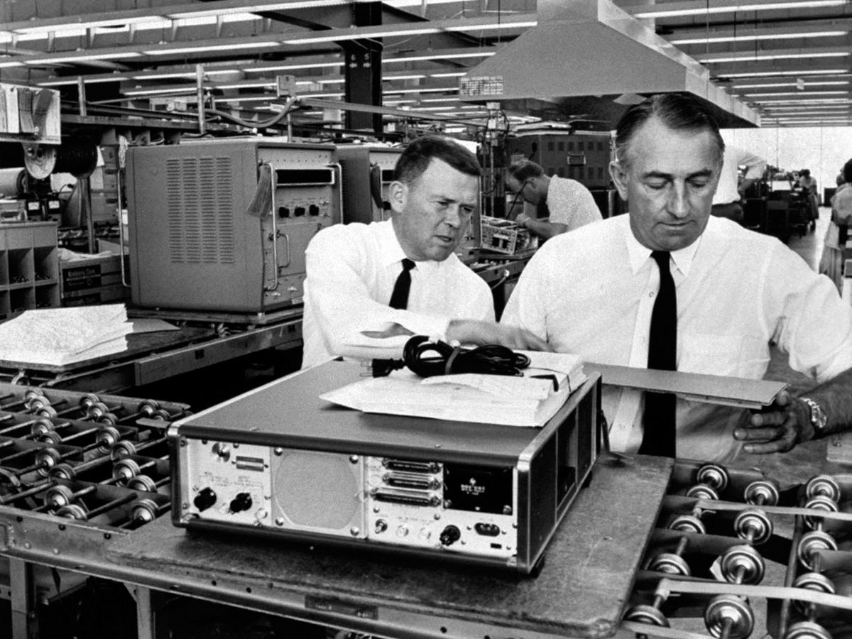 A black-and-white photo shows Hewlett Packard founders William Hewlett and David Packard in a factory.