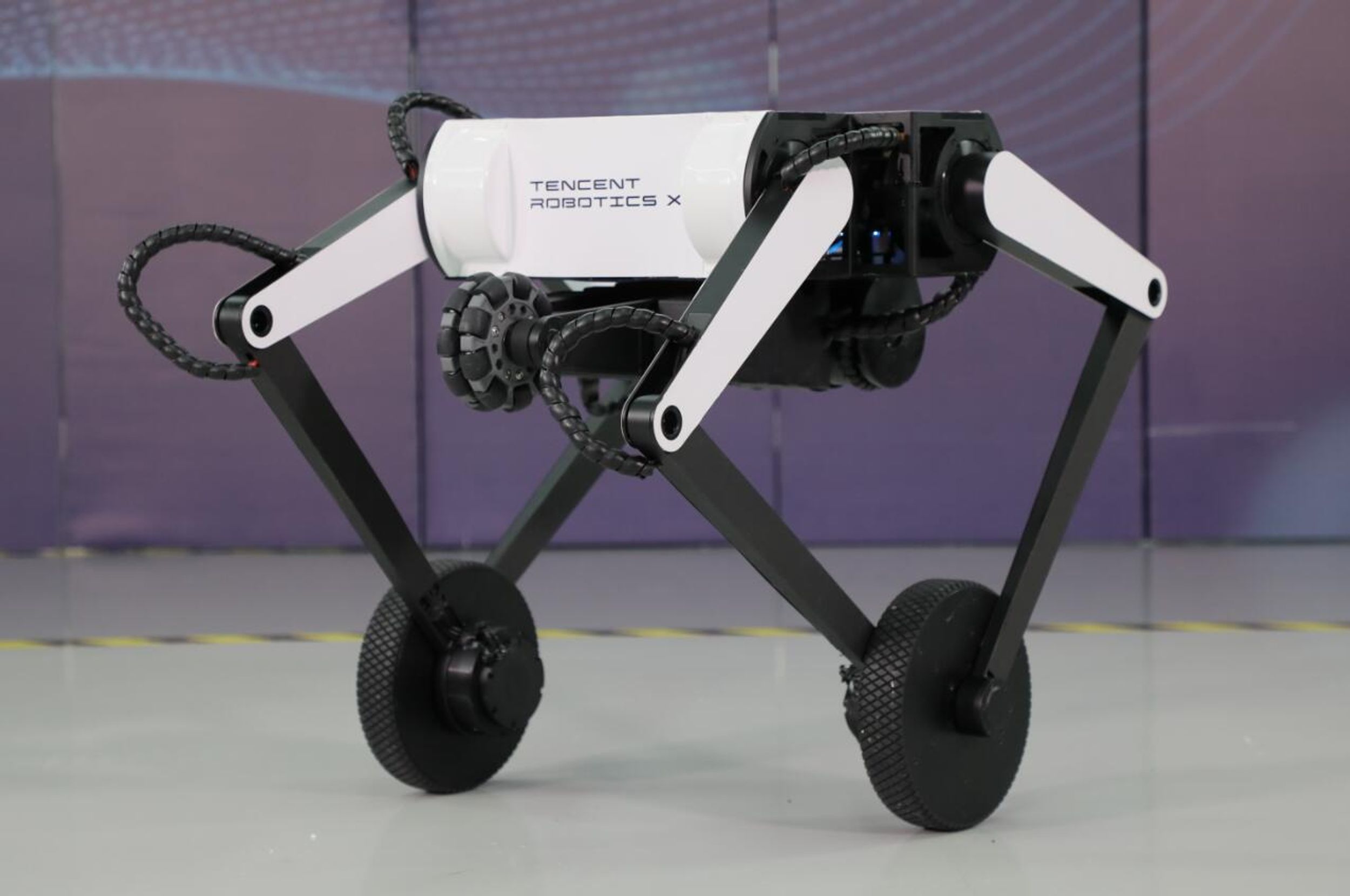 A black and white robot with four legs: each pair of legs is joined by an axle supporting a wheel. A wheeled tail is tucked up under the body.