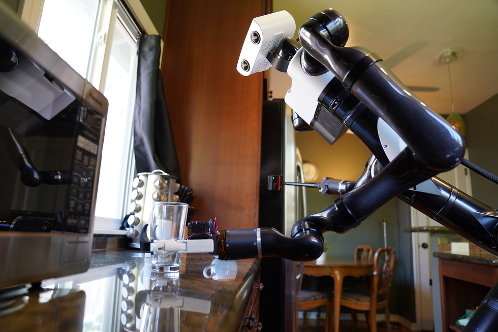 A black and white two armed robot grasps a glass in a kitchen