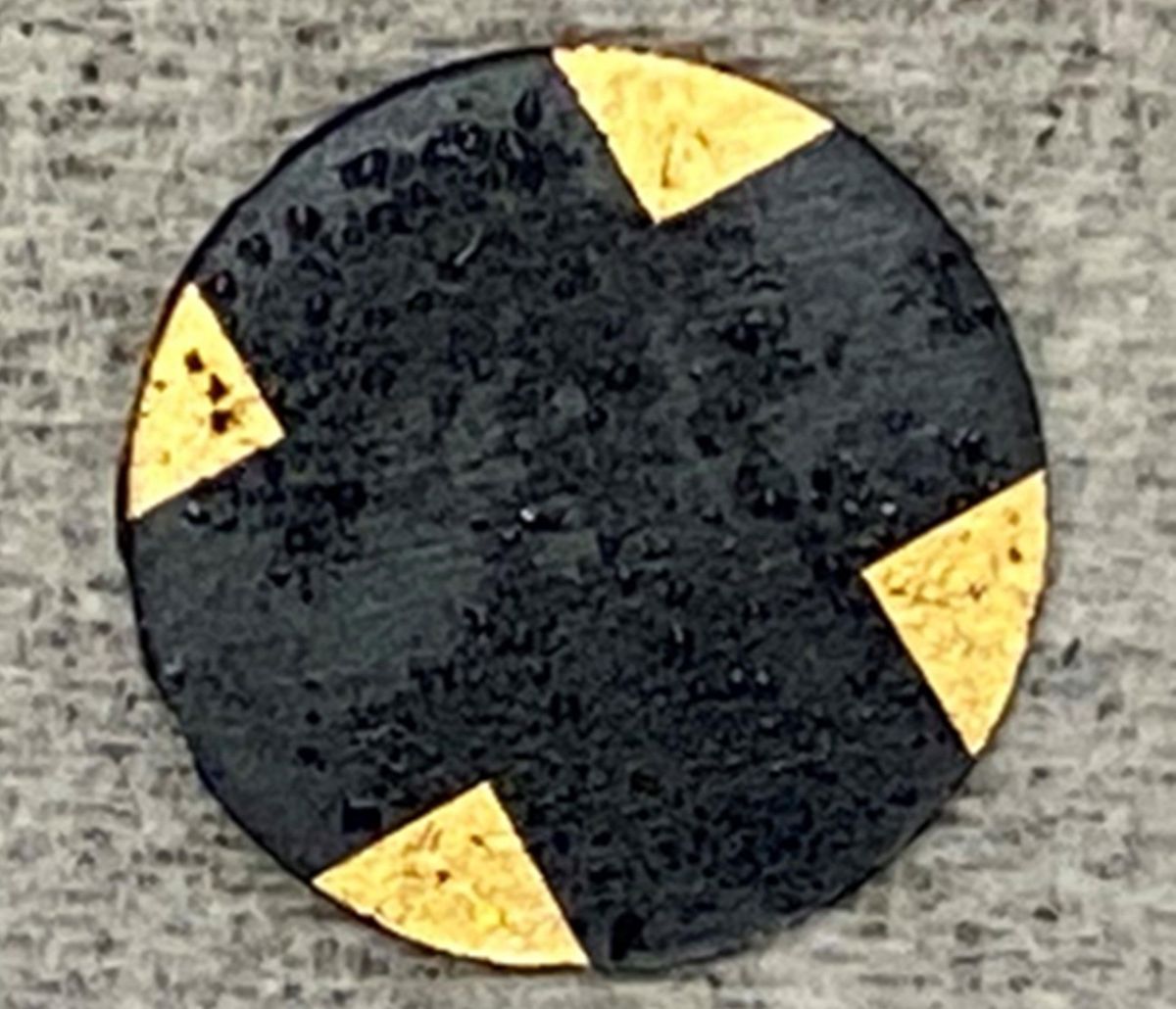 a black disc with gold nodes on the corners against a gray background 