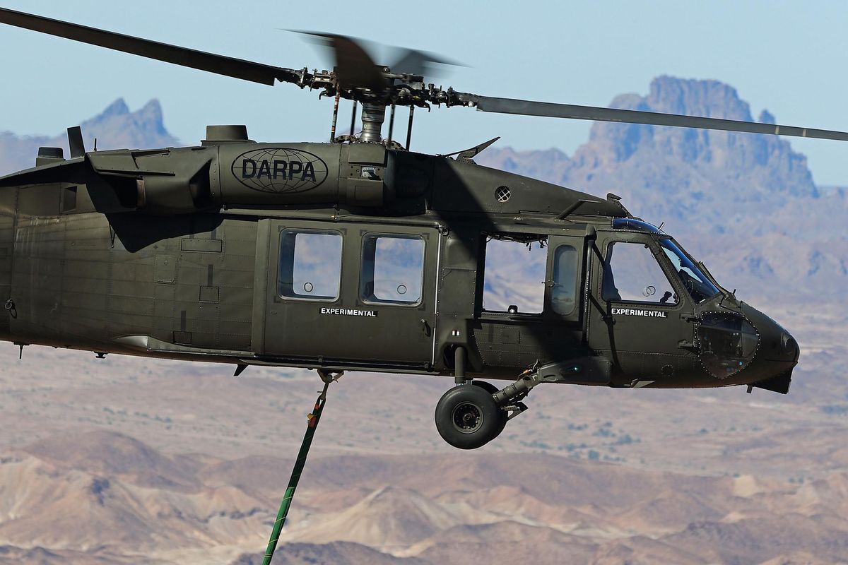 A Black Hawk helicopter with the DARPA logo on it flies over the desert with no crew on board