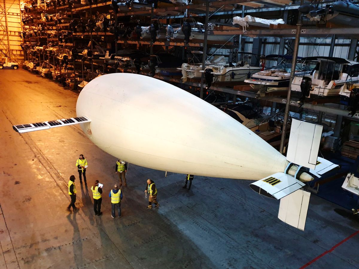 A blimp in a hanger above people.