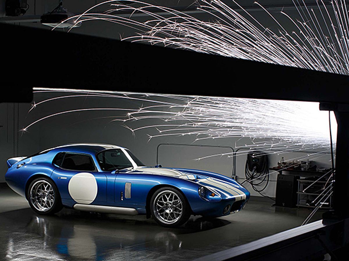 A blue and white sports car with sparks flying in front of it.