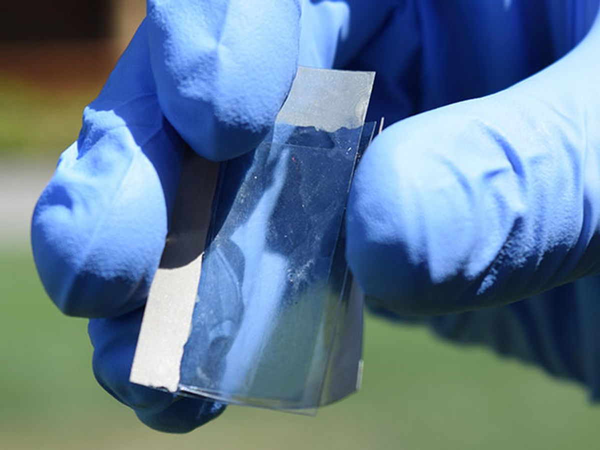 A blue-gloved hand bending a piece of silvery-plastic film containing the artificial synapse