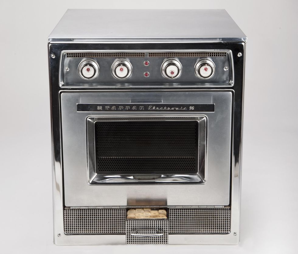 A boxy kitchen appliance housed in metal with a glass door, four white and red dials, and a small recipe drawer at the bottom.