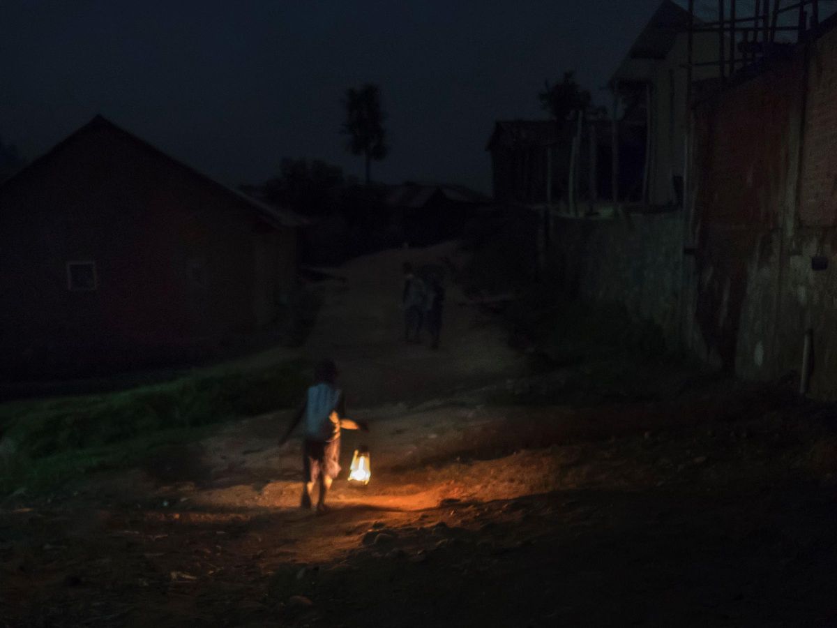 A boy walks through a dark neighborhood, lit only by his handheld oil lamp.