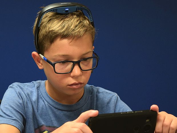 A boy wearing a headband with an EEG sensor holds a smartphone and plays a game.