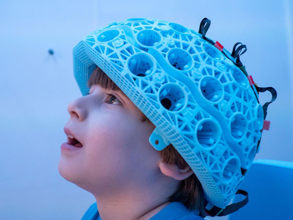 A boy wears a blue helmet on his head, fitting with cables and sensors.