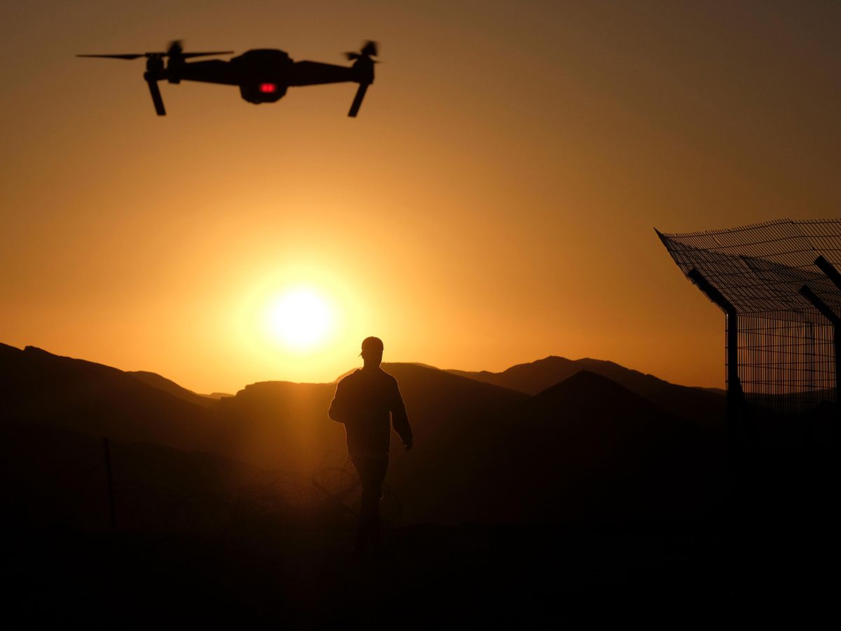 A camera equipped radio controlled quadcopter drone flying over a silhouetted man.