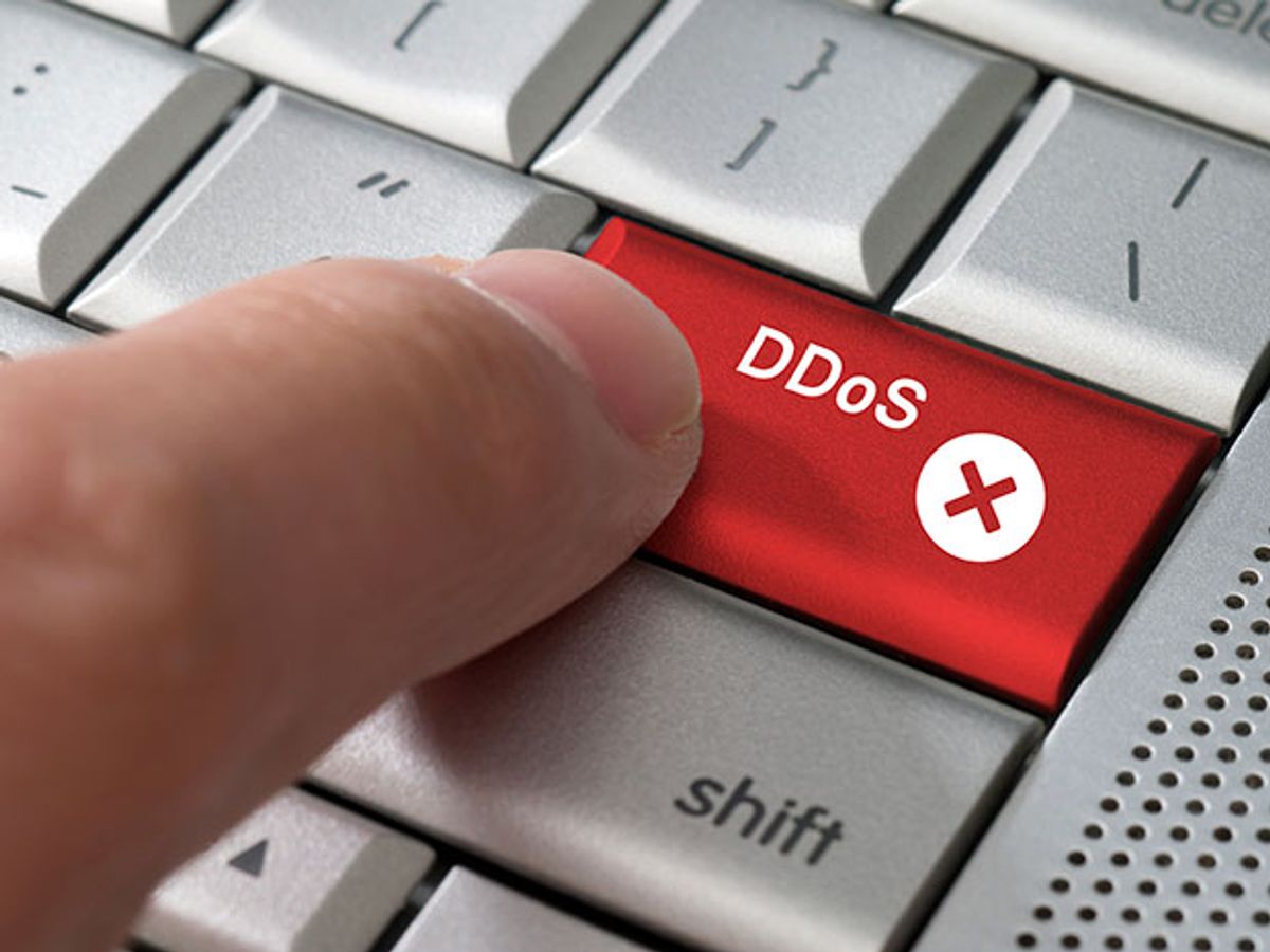 A close-up image of a finger pushing a red key titled “DDoS,” which stands for distributed denial-of-service attacks, on a white keyboard.