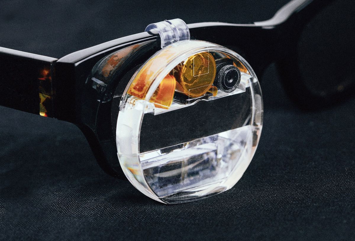 A close-up of a thick glass lens with hardware sitting on the front of a pair of glasses.