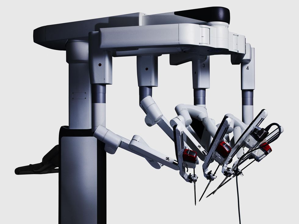 A close-up photo of a machine with four appendages hanging down from a top bar. The robotic arms are jointed and are tipped with a variety of sharp instruments.  