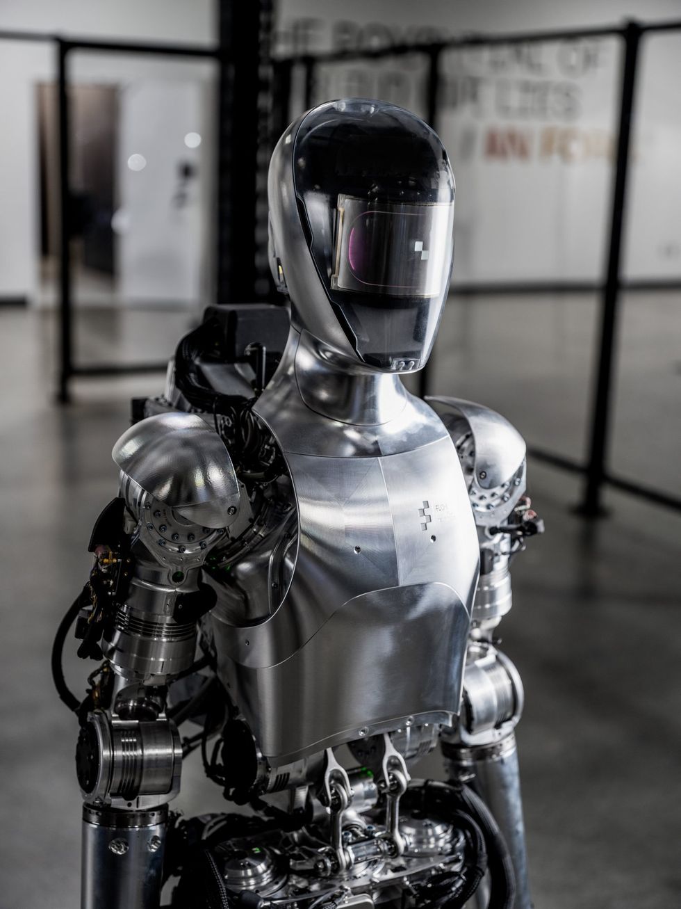 A close-up photograph of a slim humanoid robot standing with shiny metal skin and a black motorcycle helmet.
