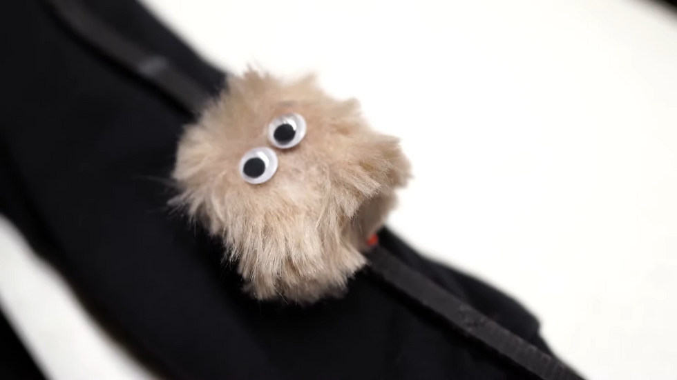 A close up photograph of a small puffy robot with googly eyes climbing on a sleeve