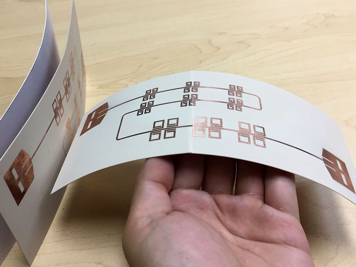 A close-up shows the size of printed thin, flexible LiveTag tags held in someone's hand in comparison with a piece of photo paper on the far left.