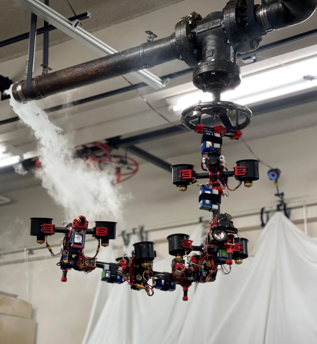 A complex aerial robot made of multiple segments of actuators and ducted fans grasps and turns a valve near a ceiling