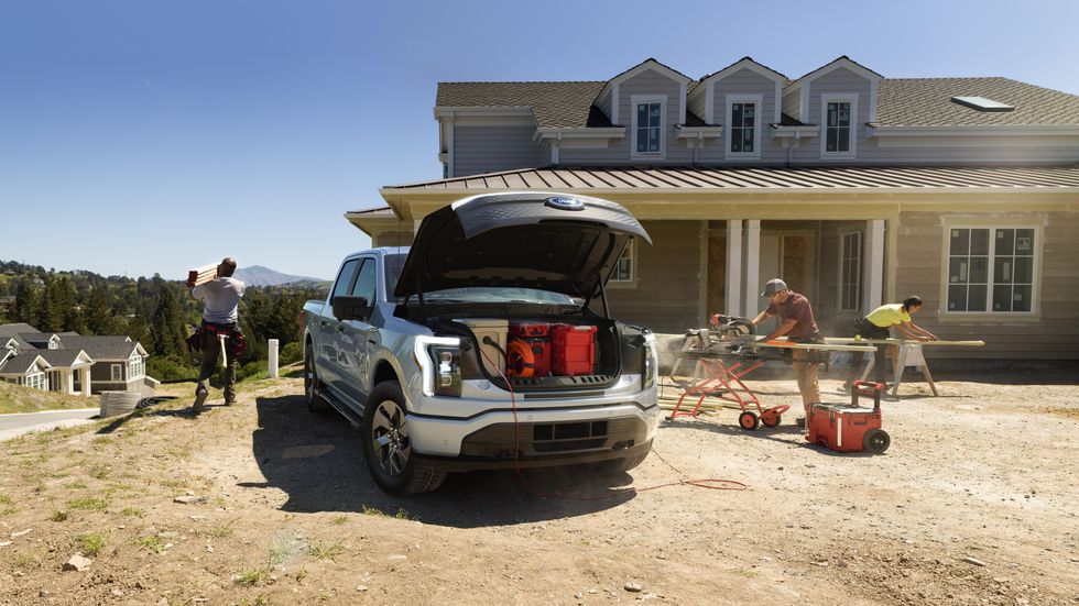 A construction crew working on a site with a Ford F-150's frunk open showing tools.