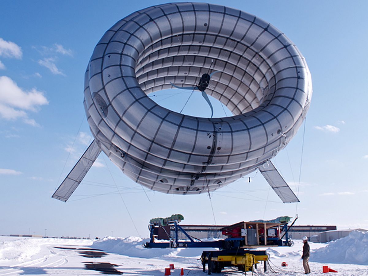 A cylindrical balloon with fins floats above snowy ground.