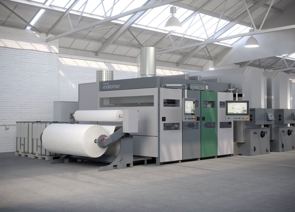 A digital textile printing machine consisting of multiple cabinets attached to a large roll of fabric stands on a gray and white warehouse.
