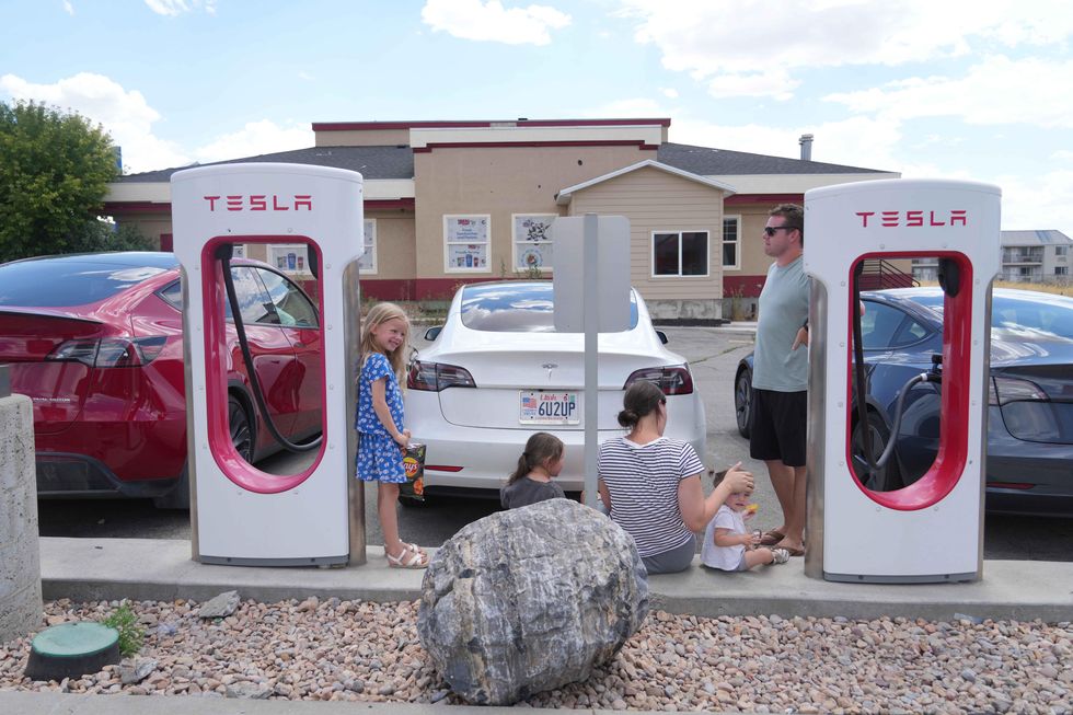 A family eats snacks while waiting in 100 degree heat as their Tesla car charges on July 17, 2022 in Nephi, Utah. 