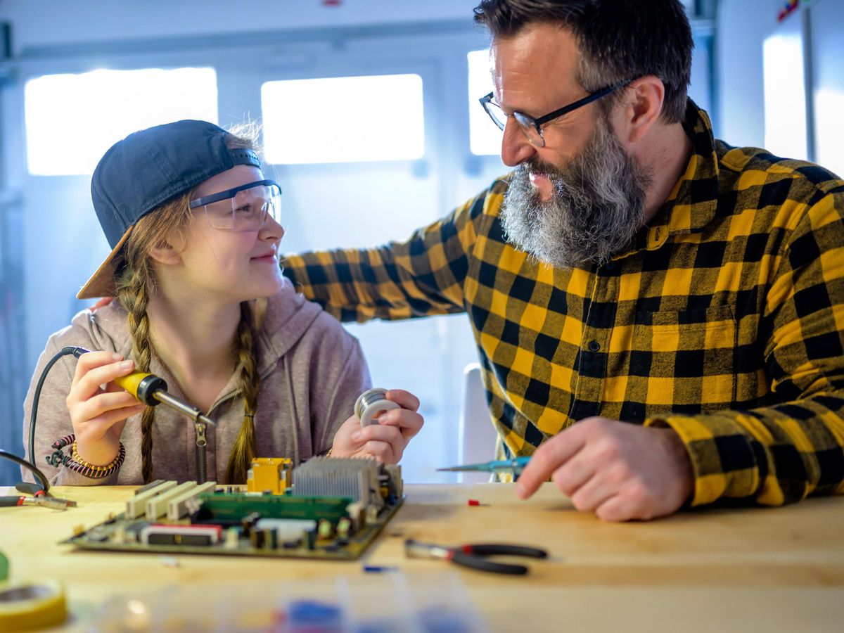 A father and daughter smiling at each other with a circuit board on a table in front.  
