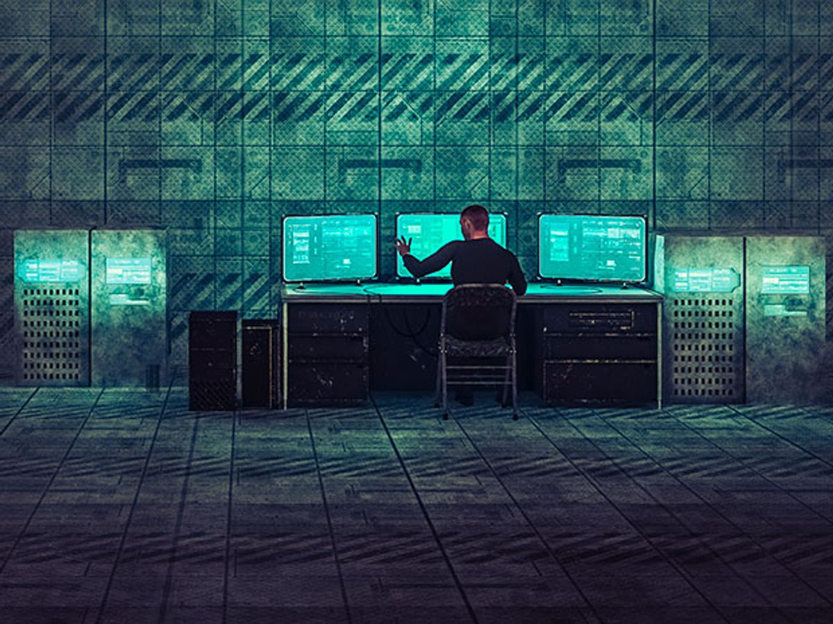 A figure in black inputs commands into a computer screen in the corner of an industrial facility.