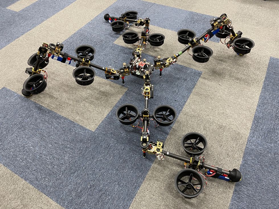 A four legged robot with thrusters on its limbs lies sprawled out on carpet