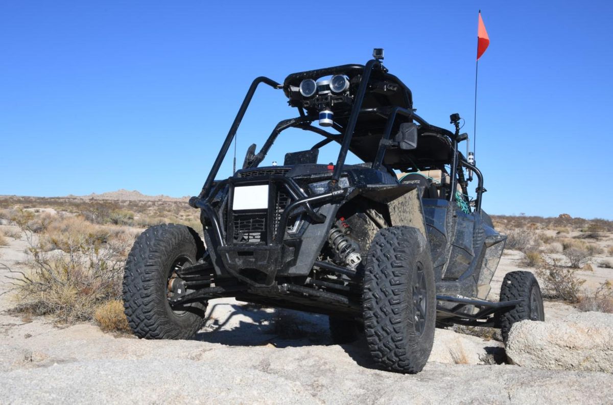 A four wheel open sided ATV with cameras and lidar installed poses on rocks in a desert landscape