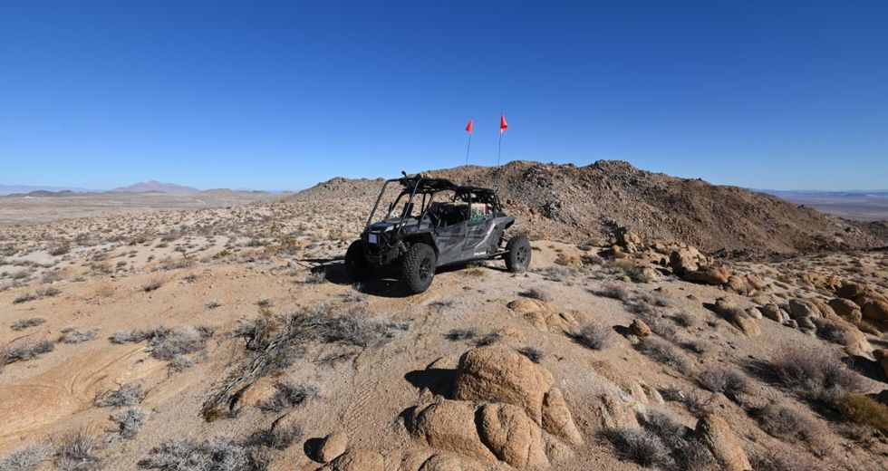 A four wheel open sided ATV with cameras and lidar installed poses on top of a hill in a desert landscape