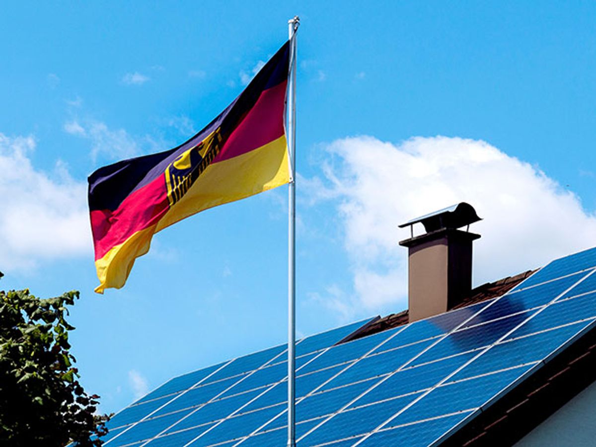 A German flag with the coat of arms flies in front of a home with solar panels