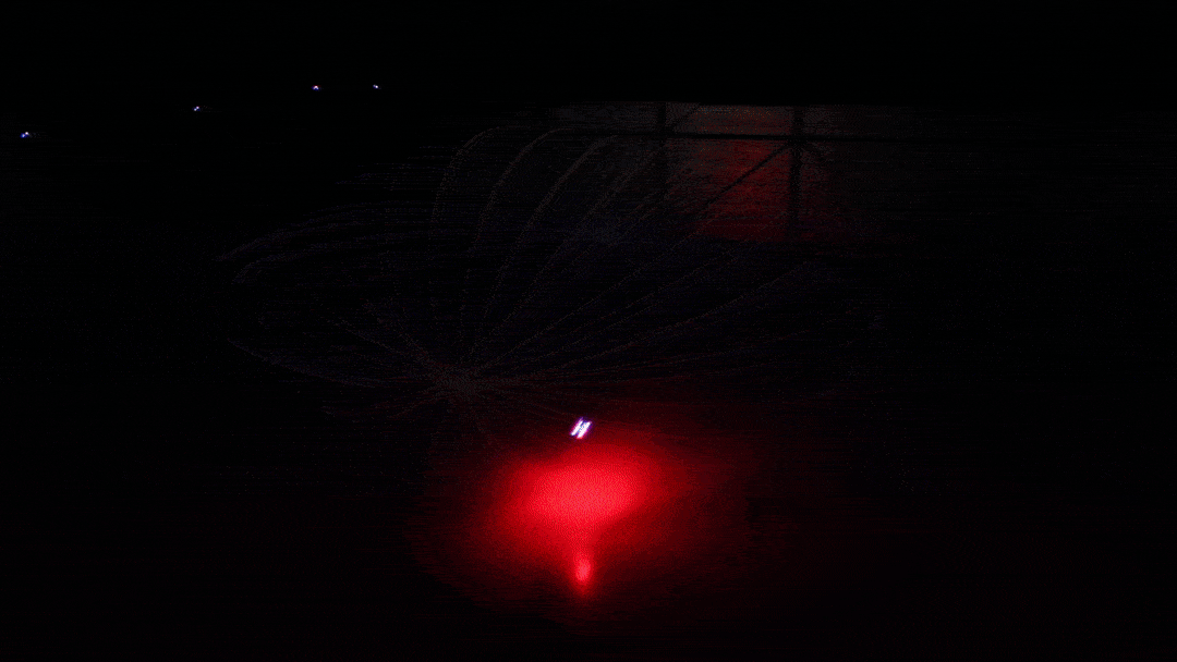 A gif showing a brightly lit drone flying a spherical pattern in a dark warehouse