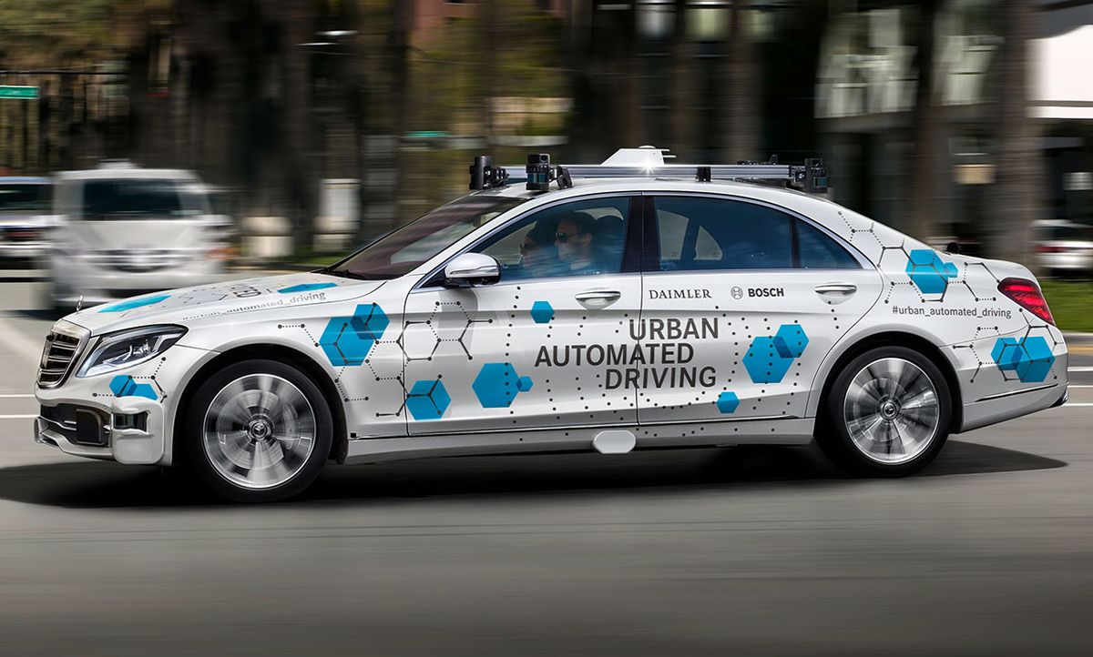 A gray car with a slogan 'Urban Automated Driving' printed on the side is shown in motion on a road. 