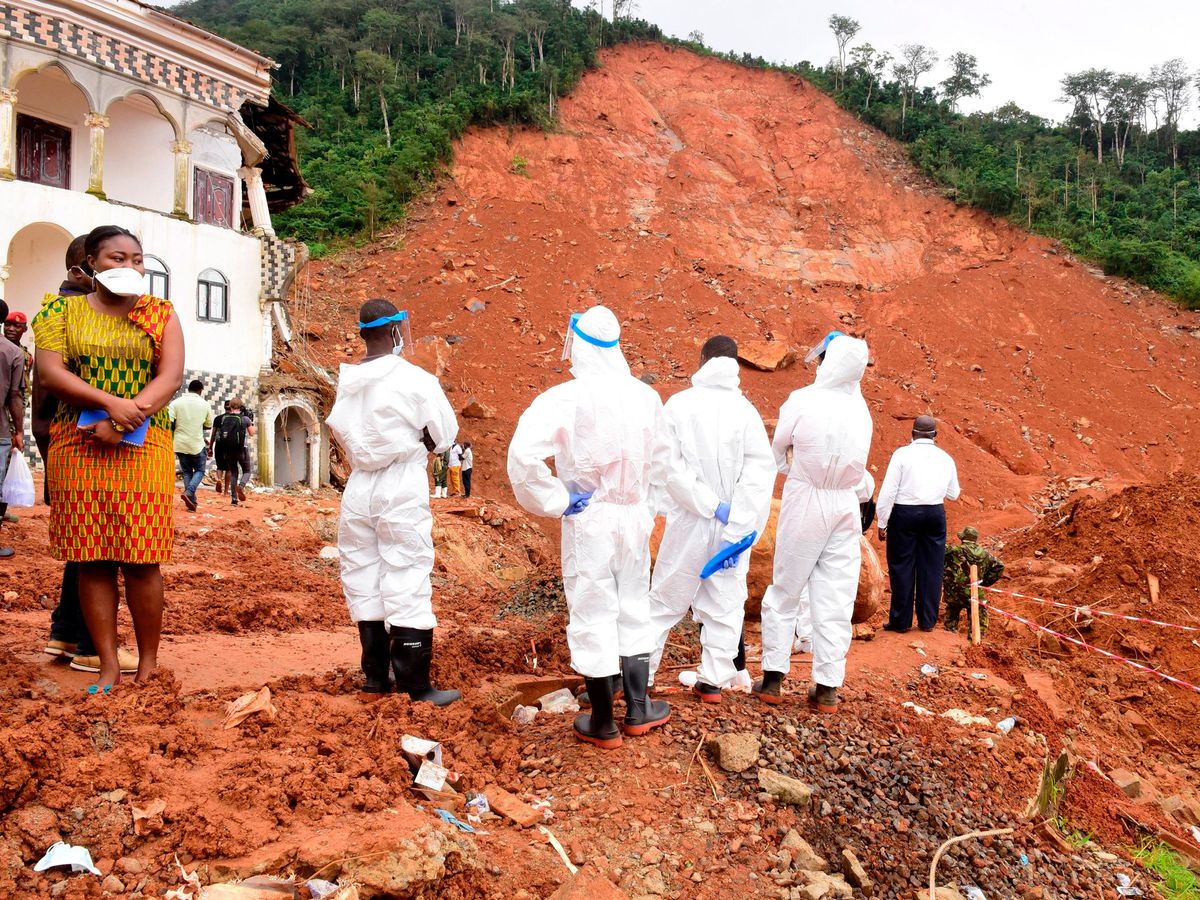 a group of people in all white suits standing at the bottom of a large hill covered in red mud