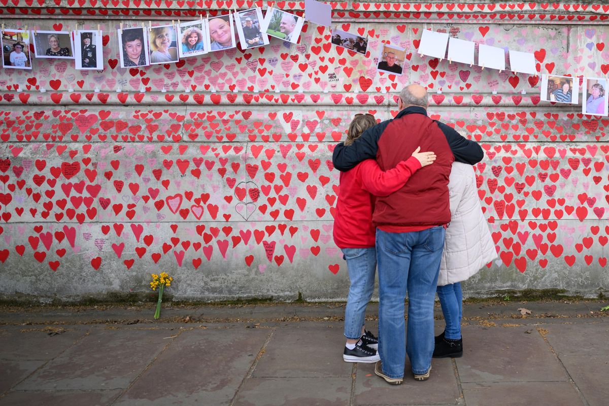 A group of people standing in front a wall with hearts on them and photos on strings above it.  