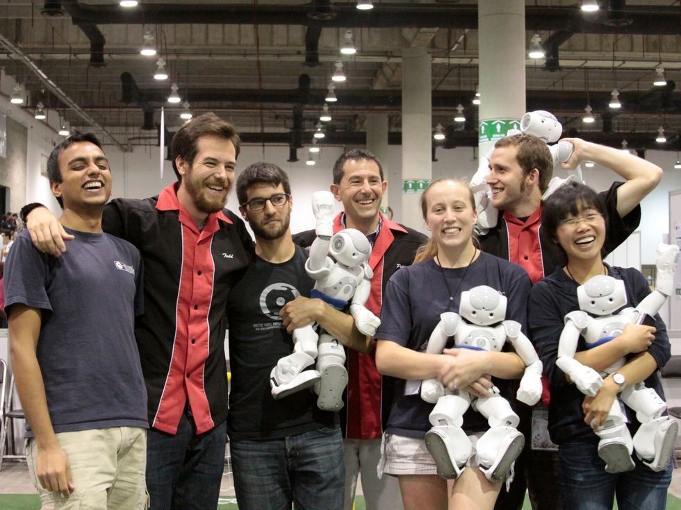 A group of smiling people holding small robots.