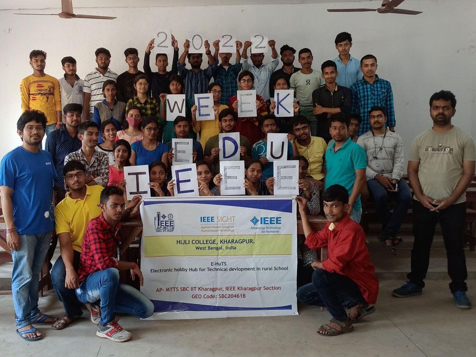 A group of students hold up signs that spell IEEE Edu Week 2022 along with a banner.