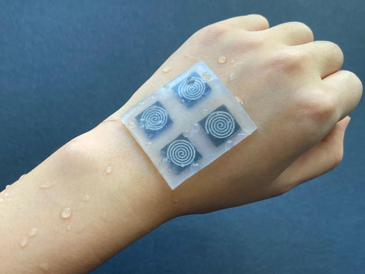 A hand covered in water droplets shows a square sheet with 4 circular sensors affixed to the top of the hand.